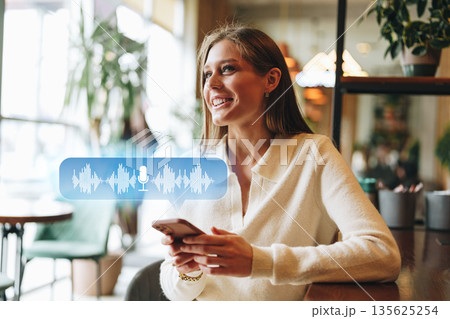 Woman enjoying time in cafe while using smartphone for voice messaging 135625254