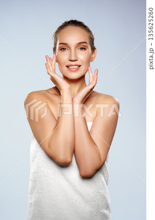 Woman poses with hands on her face in a simple studio setting with a light background 135625260