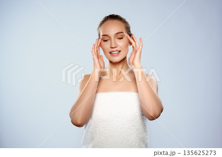 Woman applies skincare treatment while relaxing in a simple studio setting in the morning 135625273