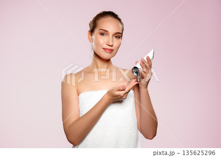 Woman applying skincare product while smiling in a bright setting 135625296