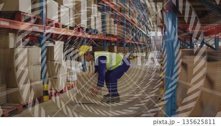 Kneeling worker wearing hard hat, safety vest lifting cardboard box on pallets in warehouse aisle Kneeling worker wearing hard hat, safety vest lifting cardboard box on pallets in warehouse aisle 135625811
