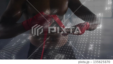 Wrapping shirtless boxer tightening red hand wraps inside gym room, with white binary code overlay Wrapping shirtless boxer tightening red hand wraps inside gym room, with white binary code overlay 135625870