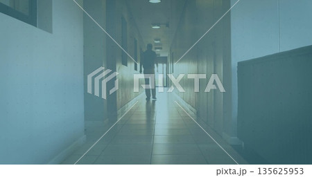 Walking senior male in dark suit along wood-panel hallway, with recessed lights and bench 135625953