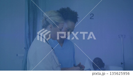 Medical staff wearing white coat, blue scrubs, stethoscope reading tablet at bedside with IV stand Medical staff wearing white coat, blue scrubs, stethoscope reading tablet at bedside with IV stand 135625956