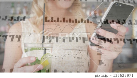 Sipping adult woman holding smartphone and analyzing overlay charts in kitchen, with smoothie jar Sipping adult woman holding smartphone and analyzing overlay charts in kitchen, with smoothie jar 135625971