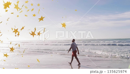 Walking mature man in white T-shirt and red shorts along wet shoreline, with golden confetti 135625974
