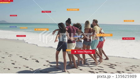 Walking group of seven friends along beach shoreline, with footprints and ocean waves 135625989