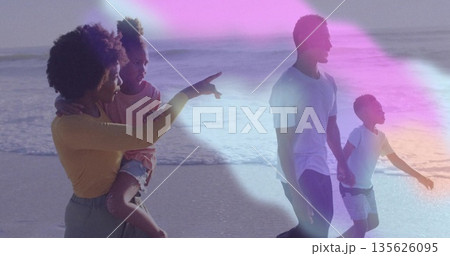 Walking family of four strolling at sandy shoreline, daughter pointing near waves and pastel light 135626095