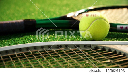 Resting yellow tennis ball nestling on overlapping racket strings over green turf court, copy space Resting yellow tennis ball nestling on overlapping racket strings over green turf court, copy space 135626108