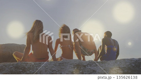 Sitting four friends gazing toward calm sea from rocky outcrop, with swimwear and bucket hat Sitting four friends gazing toward calm sea from rocky outcrop, with swimwear and bucket hat 135626138