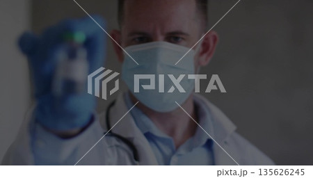 Holding medical vial, doctor wearing lab coat, surgical mask and gloves in clinic, with stethoscope 135626245
