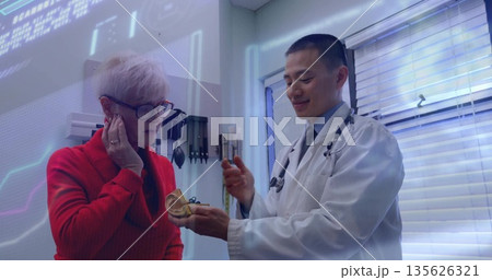 Doctor holding ear model explaining anatomy to senior patient in clinic, with stethoscope otoscope 135626321