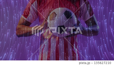 Holding classic soccer ball, athlete in red white striped jersey against purple studio backdrop Holding classic soccer ball, athlete in red white striped jersey against purple studio backdrop 135627210