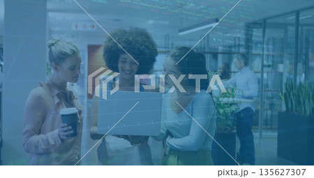 Collaborating female colleagues reviewing report on laptop at office, with coffee cup and plants 135627307