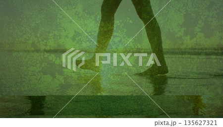 Wading woman in dark leggings through shallow water on sandy beach, with leg reflection and horizon Wading woman in dark leggings through shallow water on sandy beach, with leg reflection and horizon 135627321