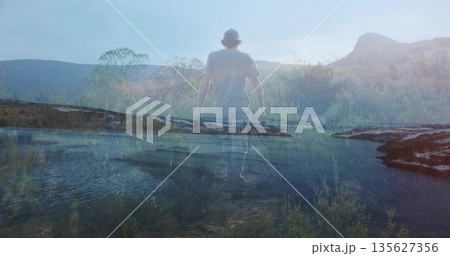 Walking man wearing t-shirt, jeans and baseball cap across shallow water at lakeshore, reflections Walking man wearing t-shirt, jeans and baseball cap across shallow water at lakeshore, reflections 135627356