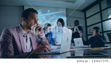 Man in blazer talking on smartphone while typing on laptop in meeting room, with projection screen Man in blazer talking on smartphone while typing on laptop in meeting room, with projection screen 135627370