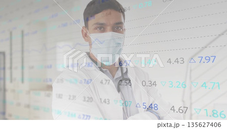 Standing Asian male doctor in lab coat tracking data in hospital corridor, with graph overlay 135627406