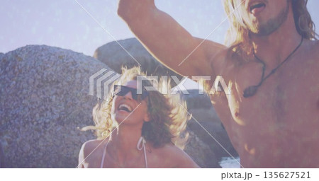 Celebrating shirtless man and woman raising arms at boulder beach, with sunglasses and bikini top 135627521