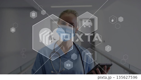 Checking tablet mid adult nurse viewing digital health icons in hospital corridor, with stethoscope 135627596