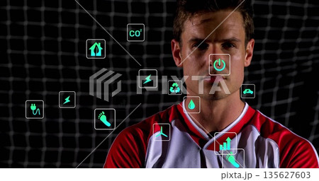 Standing male athlete wearing red white jersey in front of stadium net, with floating green icons Standing male athlete wearing red white jersey in front of stadium net, with floating green icons 135627603