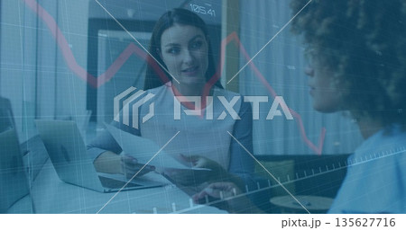 Analyzing financial charts, mid-adult woman holding documents at corporate office with laptop 135627716