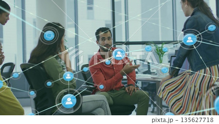 Gesturing diverse colleague wearing red shirt at office desk with monitors and network icons Gesturing diverse colleague wearing red shirt at office desk with monitors and network icons 135627718
