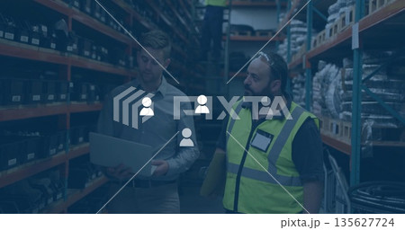 Three workers in safety gear retrieving stock on ladder in storage aisle, with laptop and documents Three workers in safety gear retrieving stock on ladder in storage aisle, with laptop and documents 135627724