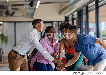 Celebrating success with high-fives, African American colleagues smiling joyfully in office 135628270