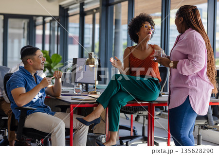 Colleagues in office discussing ideas, smiling and collaborating around desk 135628290