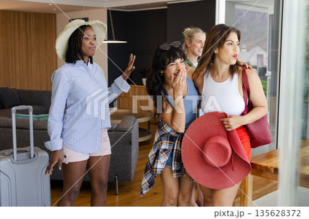 Excited diverse women arriving at vacation home with luggage, enjoying view 135628372