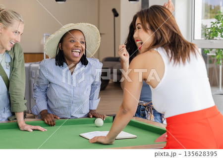 Women laughing and enjoying lively conversation around pool table indoors 135628395