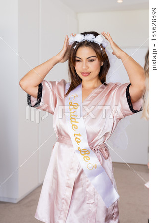Bride-to-be adjusting veil, wearing satin robe, preparing for wedding celebration 135628399