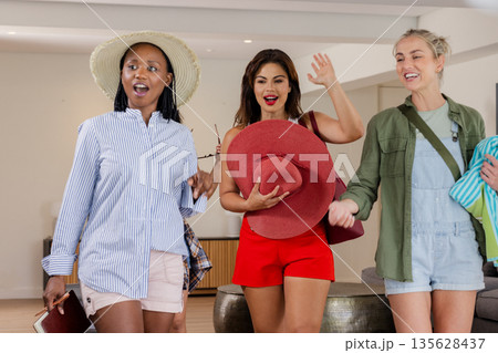Three women joyfully entering hotel lobby, holding hats and beachwear Three women joyfully entering hotel lobby, holding hats and beachwear 135628437