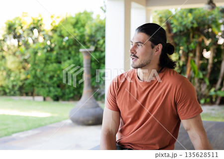 Man in orange shirt sitting outdoors, looking away thoughtfully in garden 135628511
