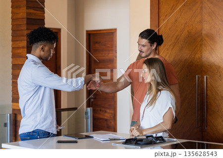 Diverse friends greeting with fist bump in modern office, smiling and connecting 135628543
