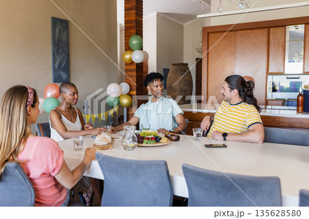 Friends enjoying conversation and sharing food at dining table in modern home Friends enjoying conversation and sharing food at dining table in modern home 135628580