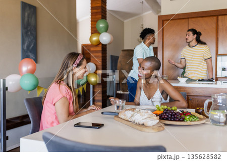 Friends enjoying conversation and snacks at home during casual gathering Friends enjoying conversation and snacks at home during casual gathering 135628582