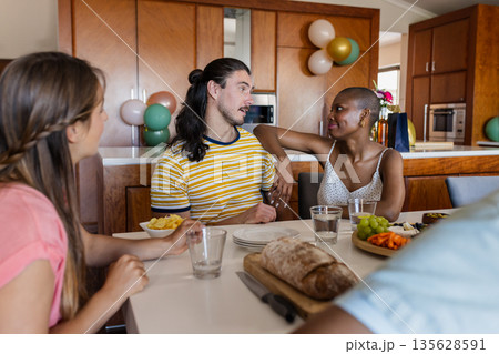 Friends enjoying conversation and snacks at home around dining table Friends enjoying conversation and snacks at home around dining table 135628591