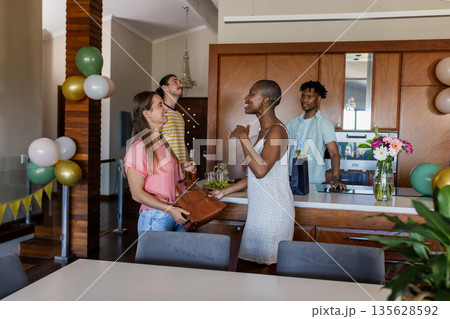 Friends gathering in modern kitchen, chatting and laughing during casual celebration Friends gathering in modern kitchen, chatting and laughing during casual celebration 135628592