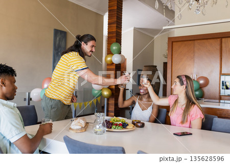 Friends toasting with drinks at dining table, enjoying celebration at home Friends toasting with drinks at dining table, enjoying celebration at home 135628596