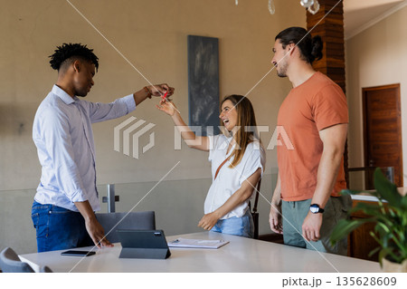 Real estate agent handing keys to excited couple in modern home Real estate agent handing keys to excited couple in modern home 135628609