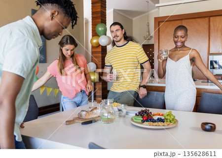 Friends enjoying snacks and drinks together at home, celebrating with joy Friends enjoying snacks and drinks together at home, celebrating with joy 135628611