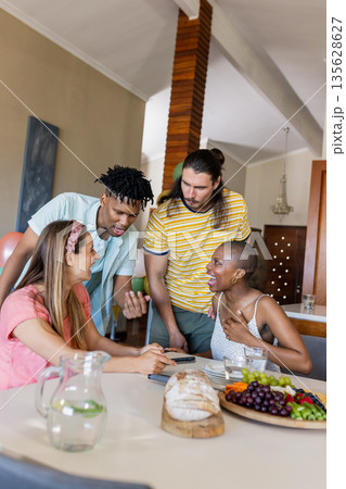 Diverse friends enjoying conversation around table with fresh fruit and bread Diverse friends enjoying conversation around table with fresh fruit and bread 135628627