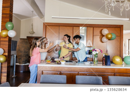 Friends toasting with drinks in modern kitchen, celebrating together with joy Friends toasting with drinks in modern kitchen, celebrating together with joy 135628634