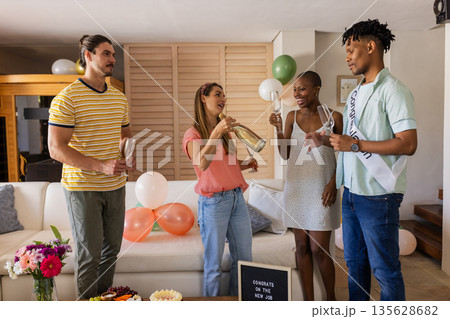 Friends celebrating new job with champagne and balloons in living room Friends celebrating new job with champagne and balloons in living room 135628682