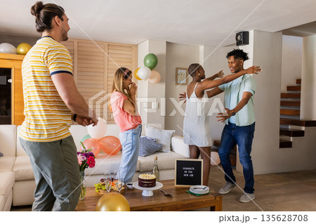 Friends celebrating birthday at home, hugging and smiling with cake and balloons 135628708