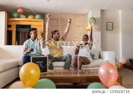 Friends celebrating new job with confetti and balloons in living room 135628710