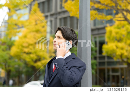 イチョウを背景にスマホを使用するスーツの男性 135629126