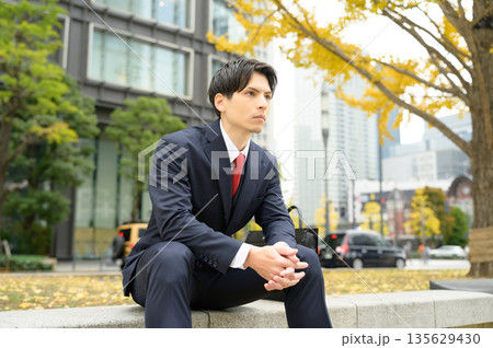 街路樹のあるオフィス街とスーツの男性 135629430